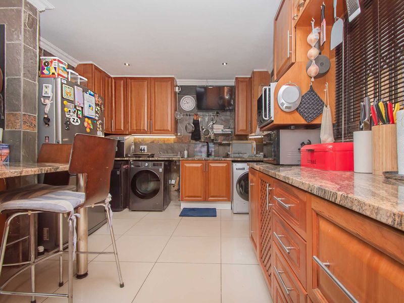 A functional kitchen featuring warm wooden cabinetry, granite countertops, stone wall accents, and integrated laundry appliances, offering a practical and well-utilized workspace.