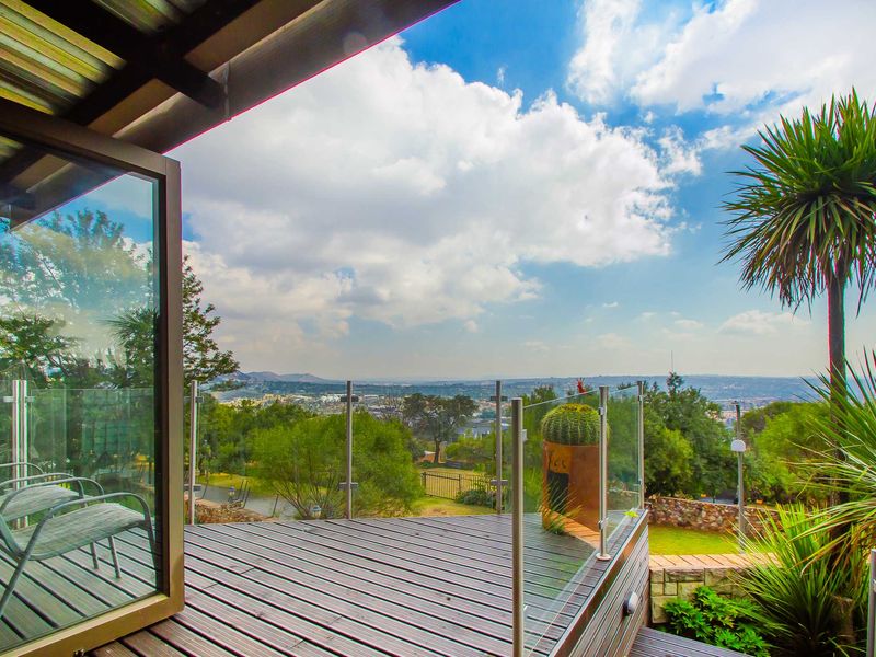 An elevated timber deck balcony featuring a modern glass balustrade and expansive panoramic views of the surrounding landscape.