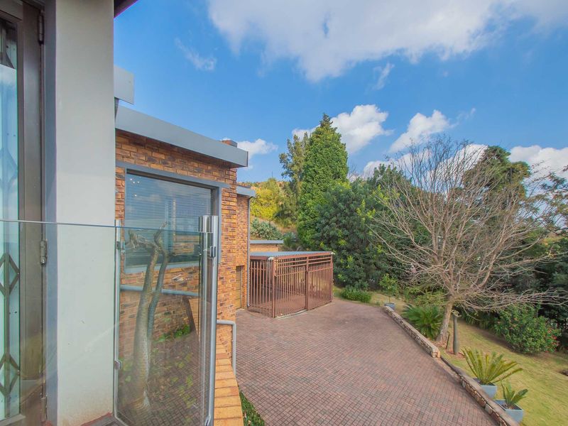 Rear exterior view featuring a brick facade, paved patio area, glass balustrade, and a secure metal enclosure set within a landscaped garden.