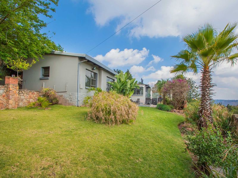 Rear view of the property featuring a well-maintained garden, stone retaining wall, and an outdoor patio area.