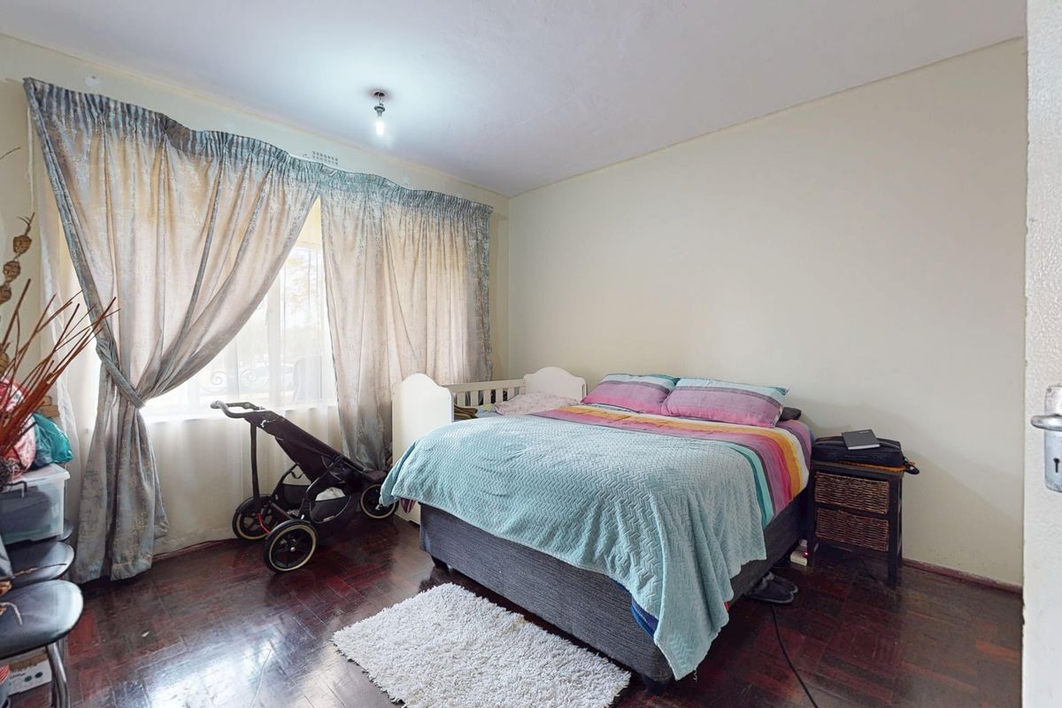 A bedroom featuring dark parquet flooring and large windows with curtain rails, offering a functional space with neutral wall finishes.