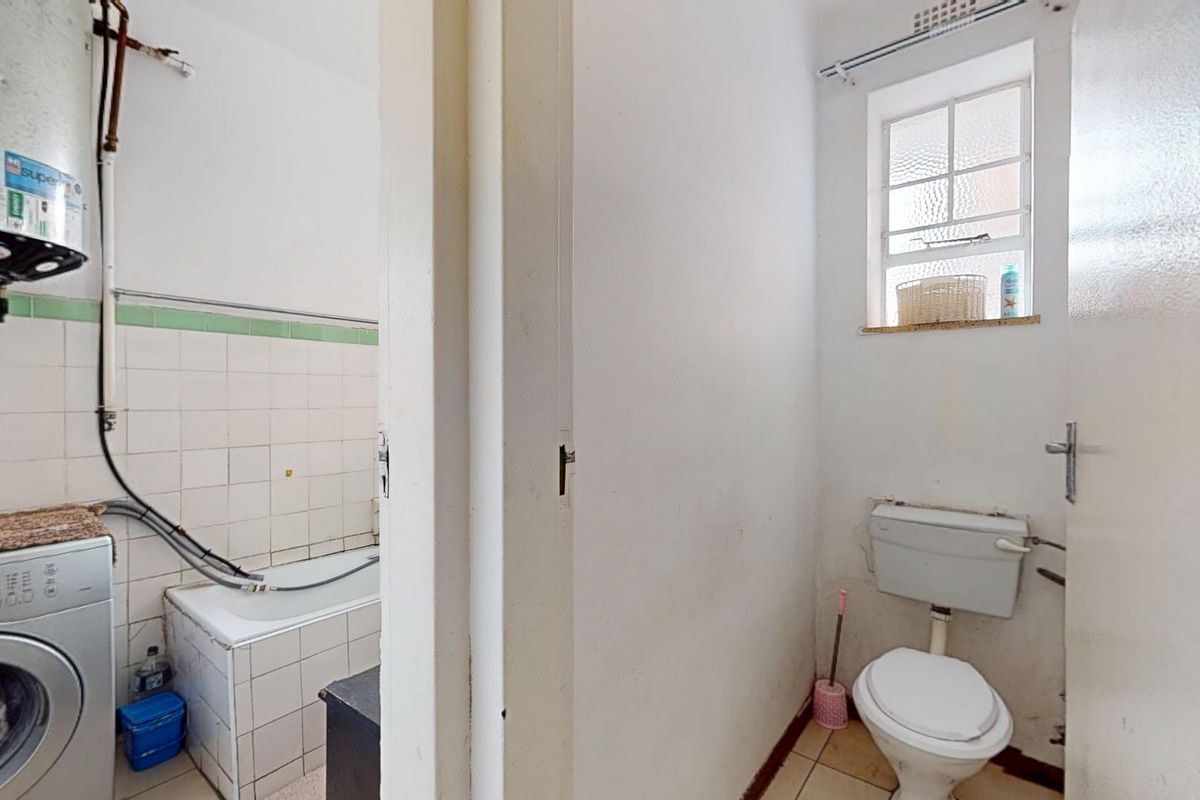 A functional bathroom and separate toilet area featuring tiled walls, a bathtub, and a window, requiring cosmetic updates to modernize the space.
