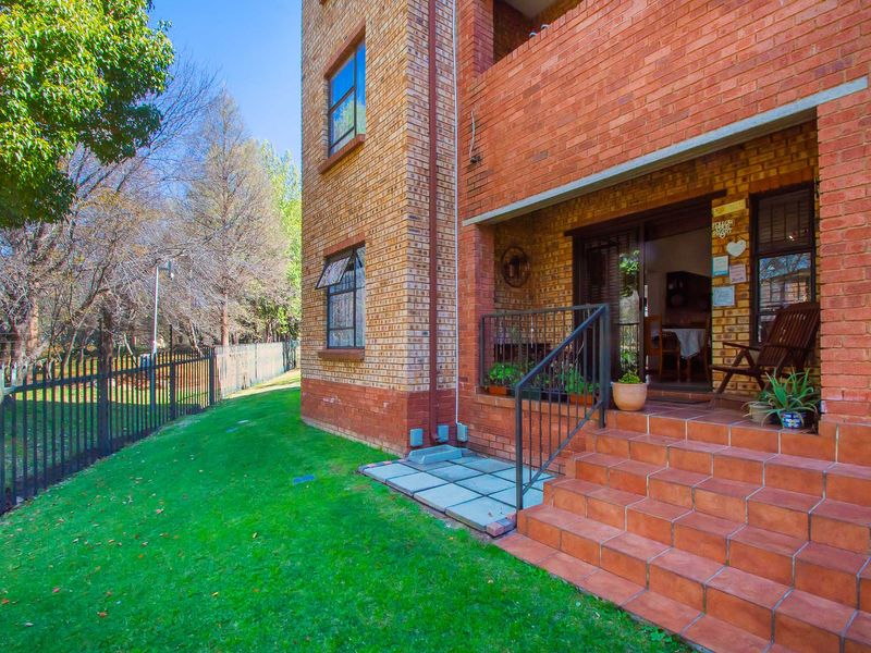Rear view of the apartment building featuring a brick facade, tiled patio steps, metal railings, and access to the garden area.