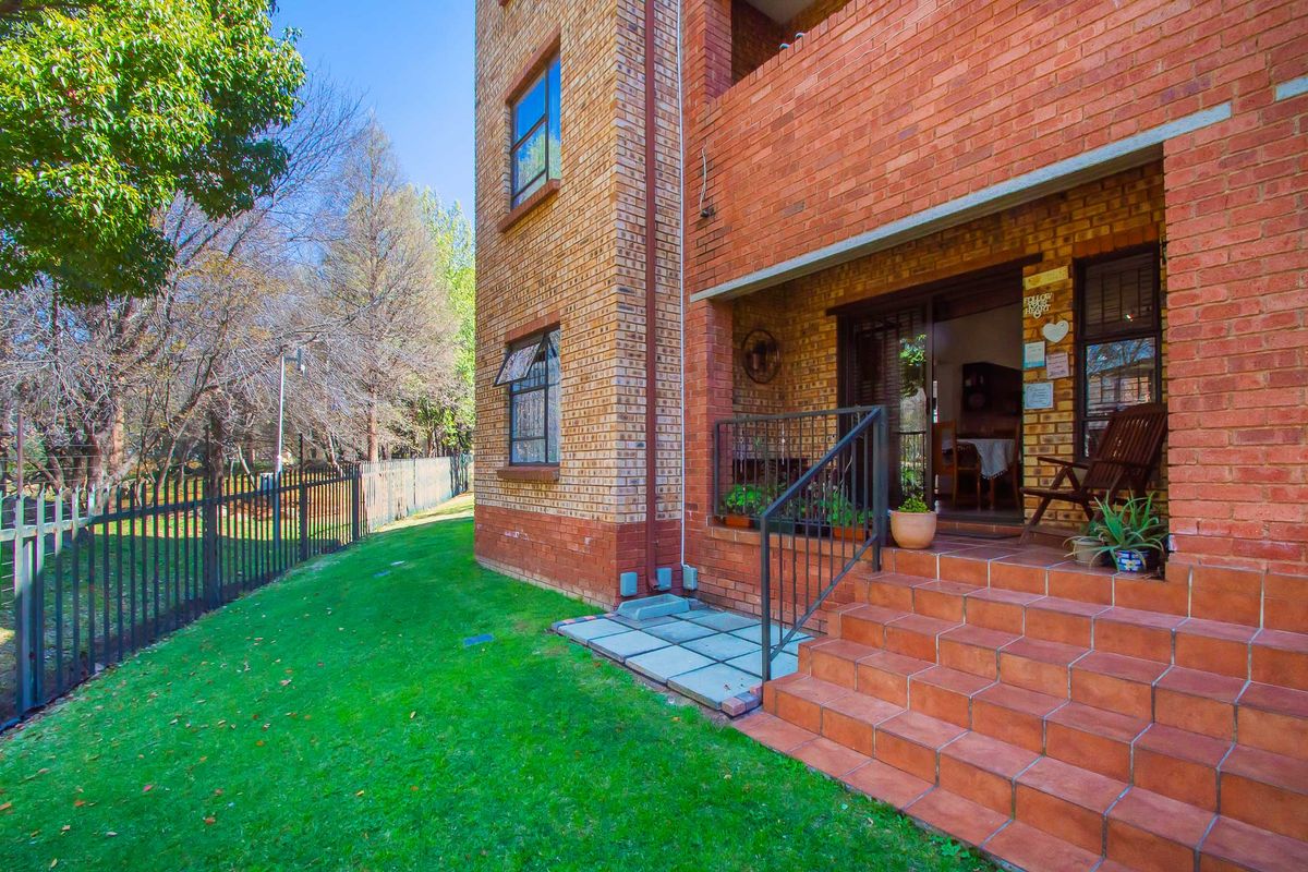 Rear view of the apartment building featuring a brick facade, tiled patio steps, metal railings, and access to the garden area.