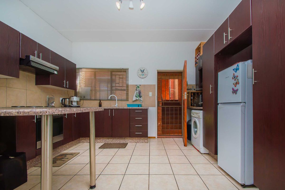 Functional kitchen featuring dark wood cabinetry, granite countertops, built-in oven, extractor fan, and tiled flooring with direct access to an exterior security gate.