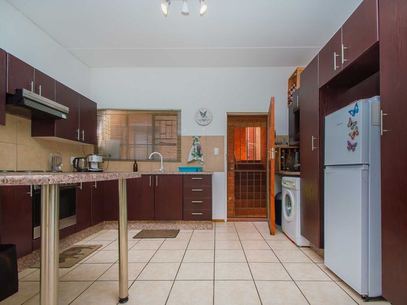 Functional kitchen featuring dark wood cabinetry, granite countertops, built-in oven, extractor fan, and tiled flooring with direct access to an exterior security gate.
