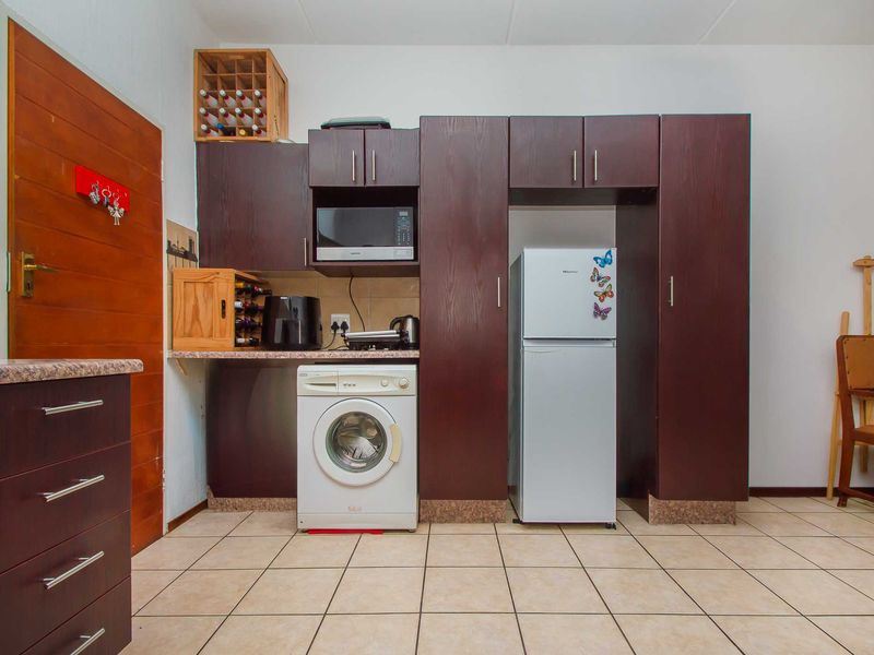 A functional kitchen area featuring dark wood-finish cabinetry, tiled flooring, and integrated space for laundry appliances and a refrigerator.