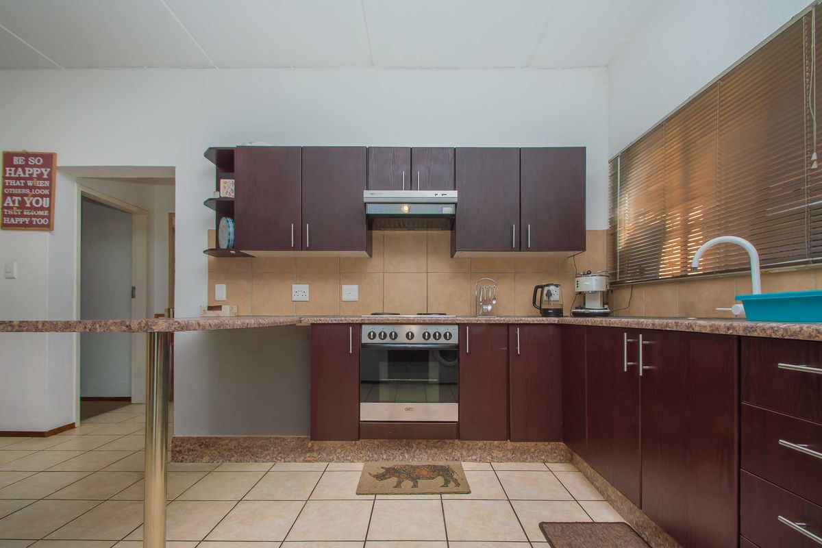 Functional kitchen featuring dark wood cabinetry, laminate countertops, built-in oven with extractor fan, and tiled flooring with an integrated breakfast bar.