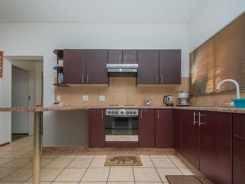 Functional kitchen featuring dark wood cabinetry, laminate countertops, built-in oven with extractor fan, and tiled flooring with an integrated breakfast bar.