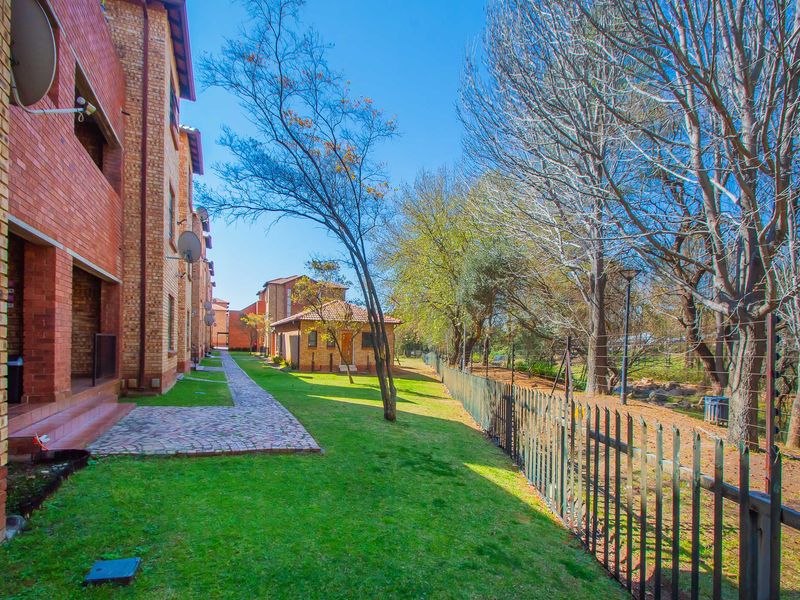 Rear view of the apartment complex featuring a brick facade, paved walkway, and well-maintained communal garden area with perimeter fencing.