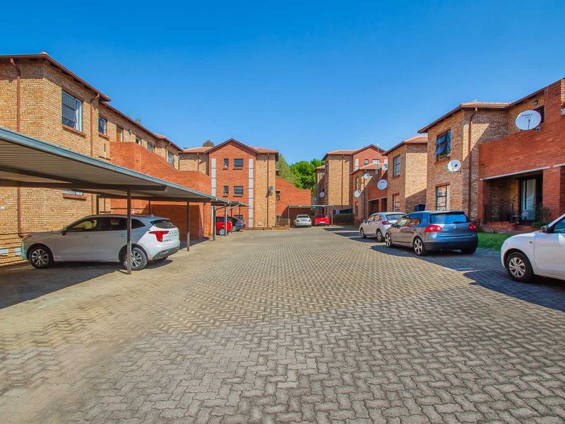 Exterior view of an apartment complex featuring brick buildings, a paved parking area, and covered carports.