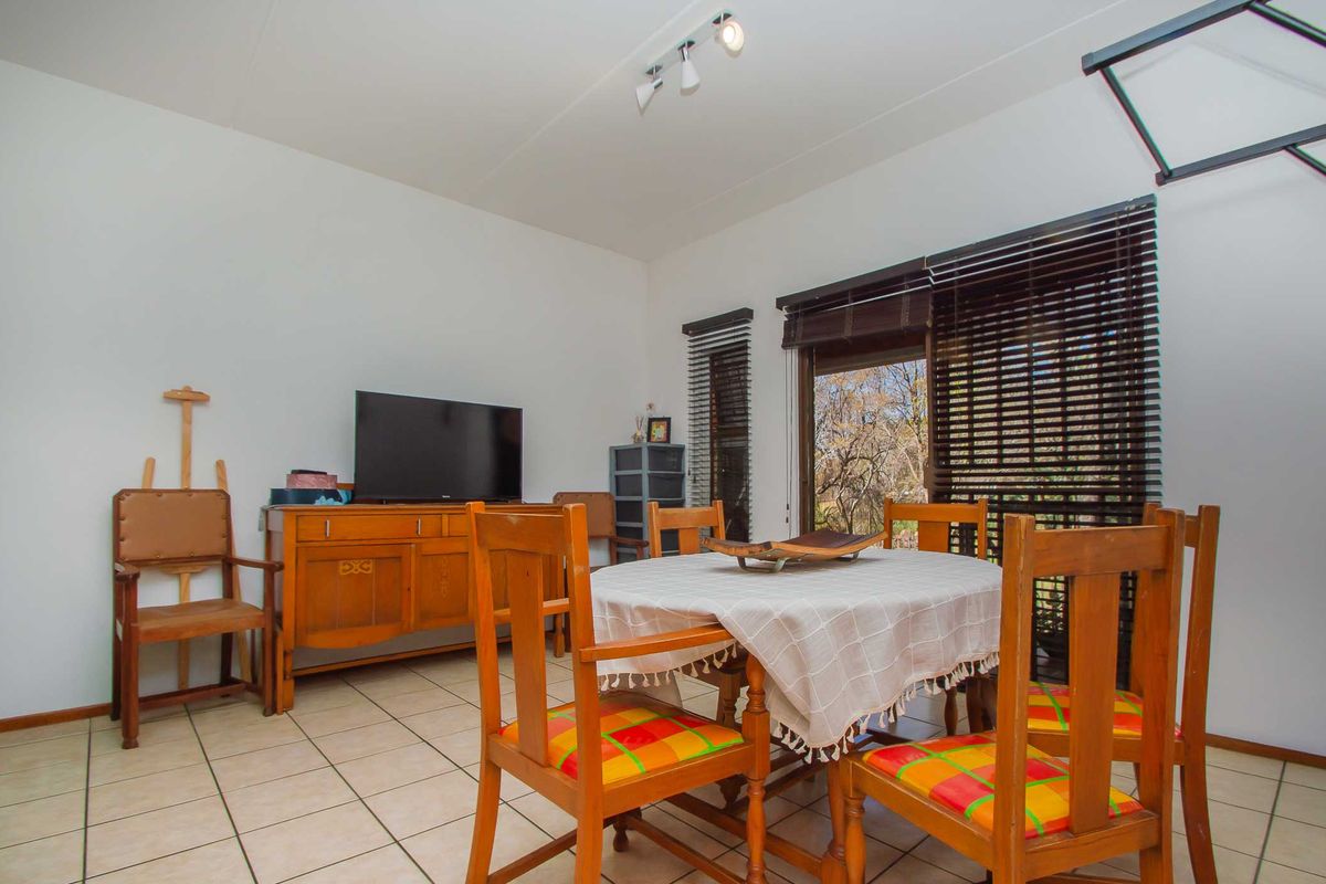 A living and dining area featuring ceramic floor tiles, track lighting, and a sliding glass door with venetian blinds providing access to the outdoors.