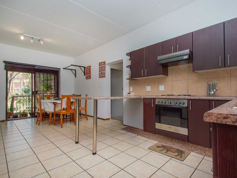 Open plan kitchen and dining area featuring dark wood cabinetry, laminate countertops, built-in oven and hob, and direct access to a balcony.