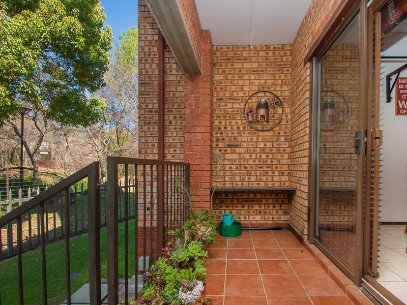 A covered patio area featuring exposed brick walls, tiled flooring, and a metal railing, providing direct access to the living space via sliding glass doors.