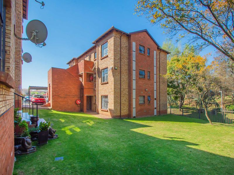 Exterior view of a multi-story face brick apartment building featuring a well-maintained lawn and secure perimeter fencing.