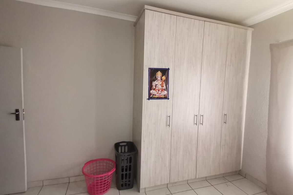 A clean bedroom featuring light-toned built-in cupboards and neutral tiled flooring, offering a functional and well-maintained space.
