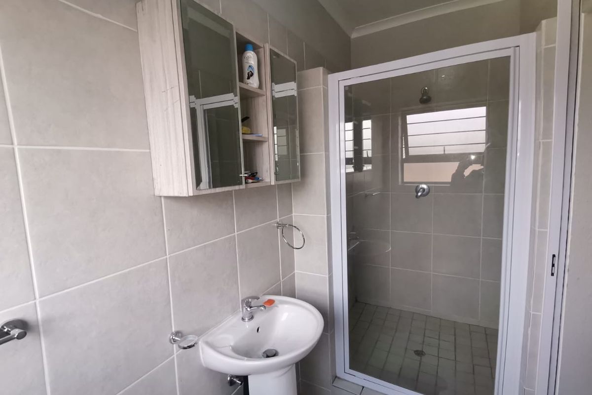 A clean, functional bathroom featuring a pedestal basin, a separate shower enclosure with a glass door, and a wall-mounted medicine cabinet.