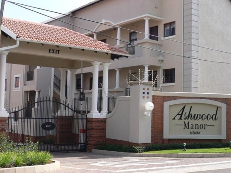 Front entrance view of Ashwood Manor apartment complex featuring a secure gated exit, brick boundary wall, and architectural columns.