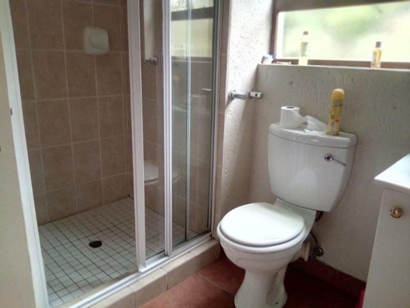 A compact bathroom featuring a shower enclosure, toilet, and tiled finishes. The space is dated and would benefit from modern updates.