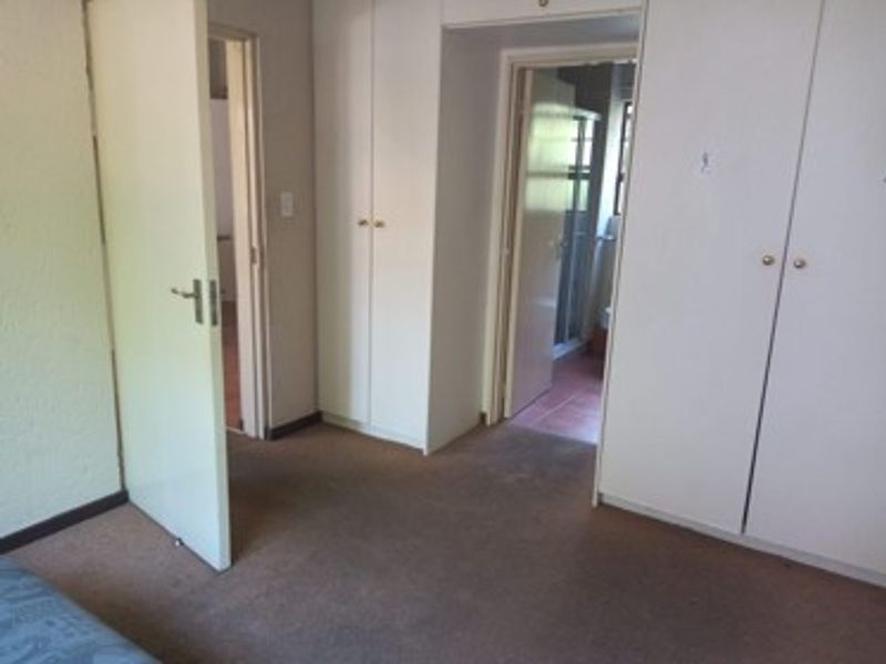 A bedroom featuring built-in cupboards and carpeted flooring, with direct access to an adjoining bathroom.