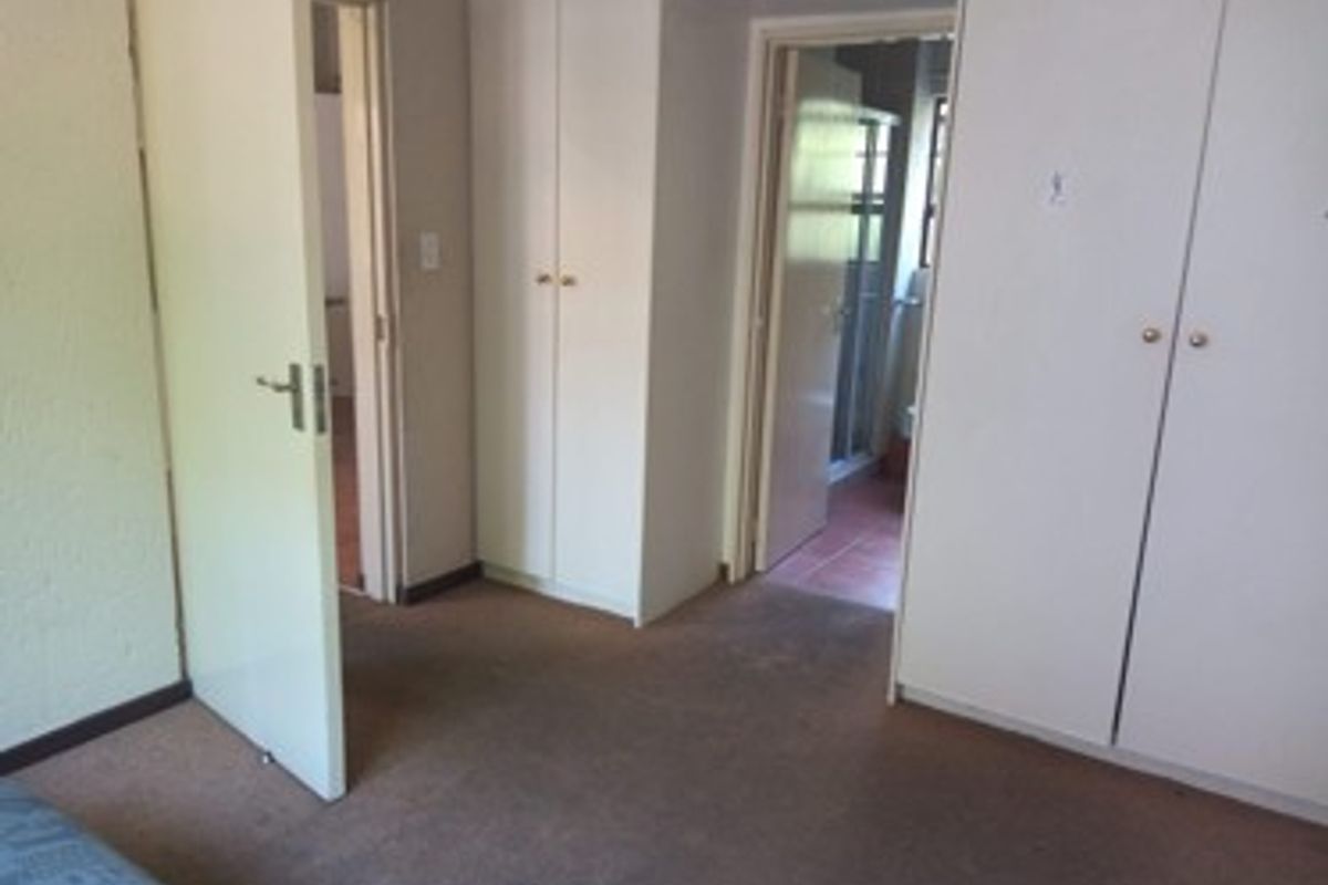 A bedroom featuring built-in cupboards and carpeted flooring, with direct access to an adjoining bathroom.