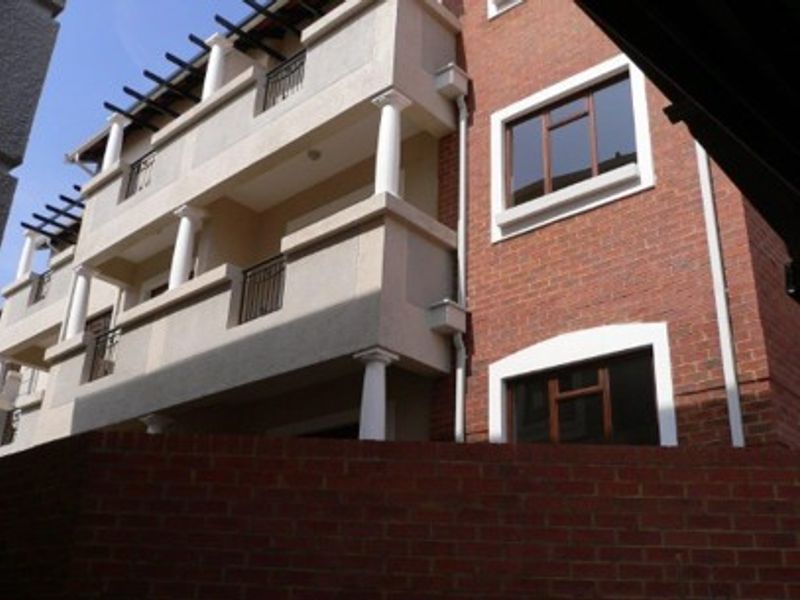 Exterior view of a multi-story apartment building featuring brick cladding, balconies with columns, and pergola structures.