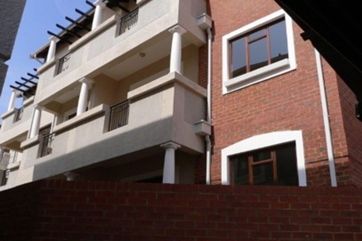 Exterior view of a multi-story apartment building featuring brick cladding, balconies with columns, and pergola structures.