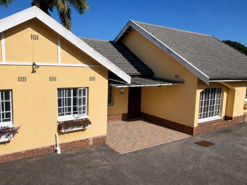 Front elevation of a single-story house featuring a tiled roof, yellow painted exterior walls, brick detailing, and a paved entrance porch.