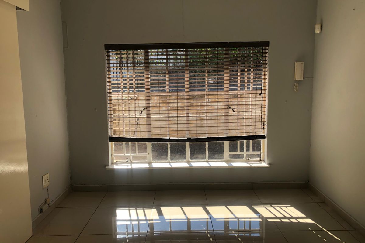 An empty bedroom featuring tiled flooring, a window with fitted blinds, and an intercom system, offering a blank canvas for personalization.