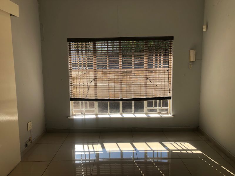 An empty bedroom featuring tiled flooring, a window with fitted blinds, and an intercom system, offering a blank canvas for personalization.