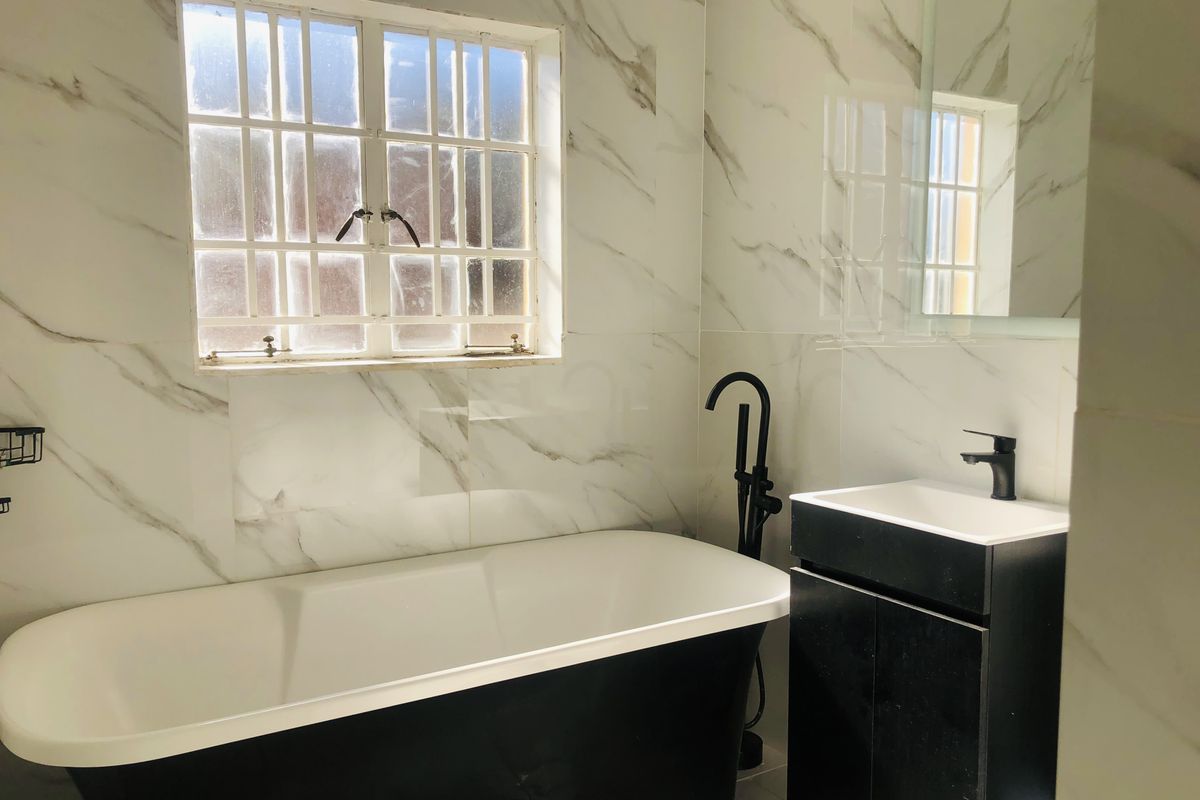 Modern bathroom featuring a sleek black freestanding bathtub, matching vanity cabinet, and elegant marble-look wall tiles.