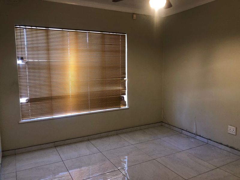 An empty bedroom featuring tiled flooring, a ceiling fan, and venetian blinds. The room requires minor finishing work around the baseboards and electrical points.
