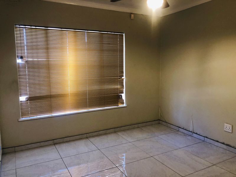 An empty bedroom featuring tiled flooring, a ceiling fan, and a window fitted with venetian blinds.