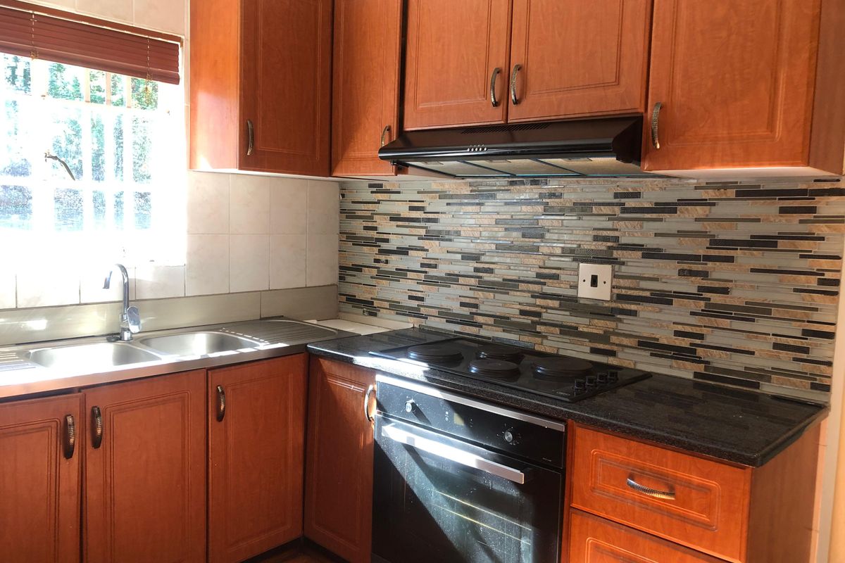 A functional kitchen featuring wooden cabinetry, a built-in oven with electric hob, extractor fan, and a modern tiled backsplash.