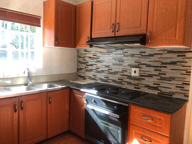 A functional kitchen featuring wooden cabinetry, a built-in oven with electric hob, extractor fan, and a modern tiled backsplash.