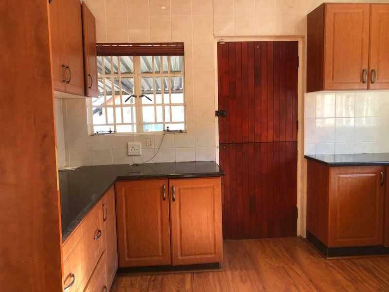 A functional kitchen featuring wooden cabinetry, dark granite countertops, tiled backsplash, and a secure window, offering a practical layout ready for modernization.