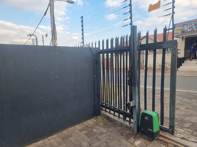 Front entrance featuring a sliding gate with an automated motor, electric fencing, and a paved driveway area.