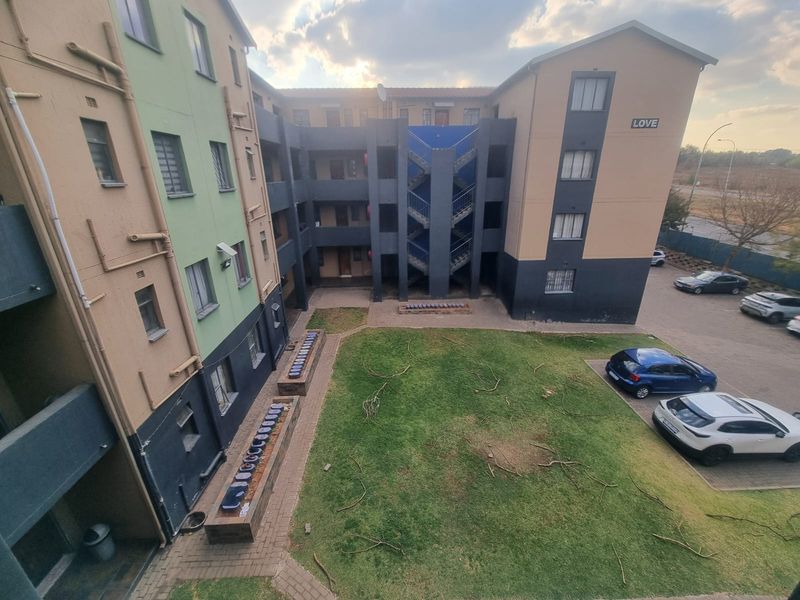 An elevated view of the apartment complex courtyard featuring a communal garden, paved walkways, and external stairwell access.