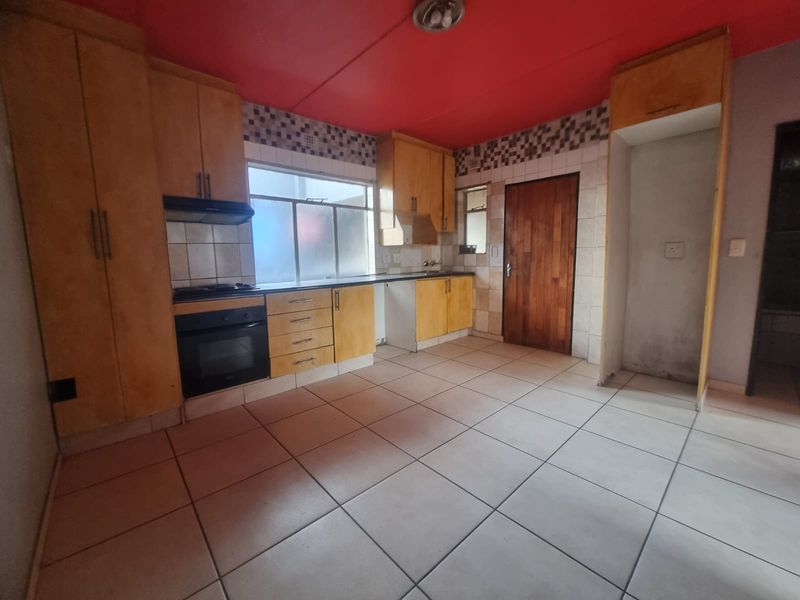 A functional kitchen featuring built-in wooden cabinetry, tiled flooring, a built-in oven and hob, and a dedicated space for a refrigerator.
