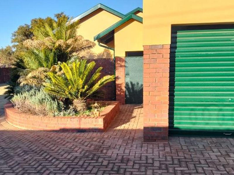 Front exterior view of the property featuring a brick driveway, a green roller garage door, and a landscaped brick planter box.
