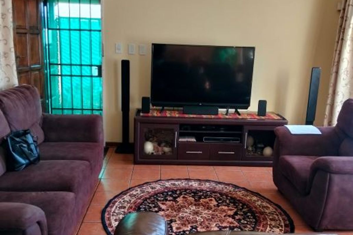 A living room featuring tiled flooring, a timber entrance door, and a security gate, providing a functional and accessible living space.
