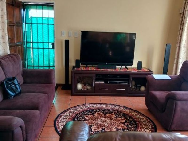 A living room featuring tiled flooring, a timber entrance door, and a security gate, providing a functional and accessible living space.