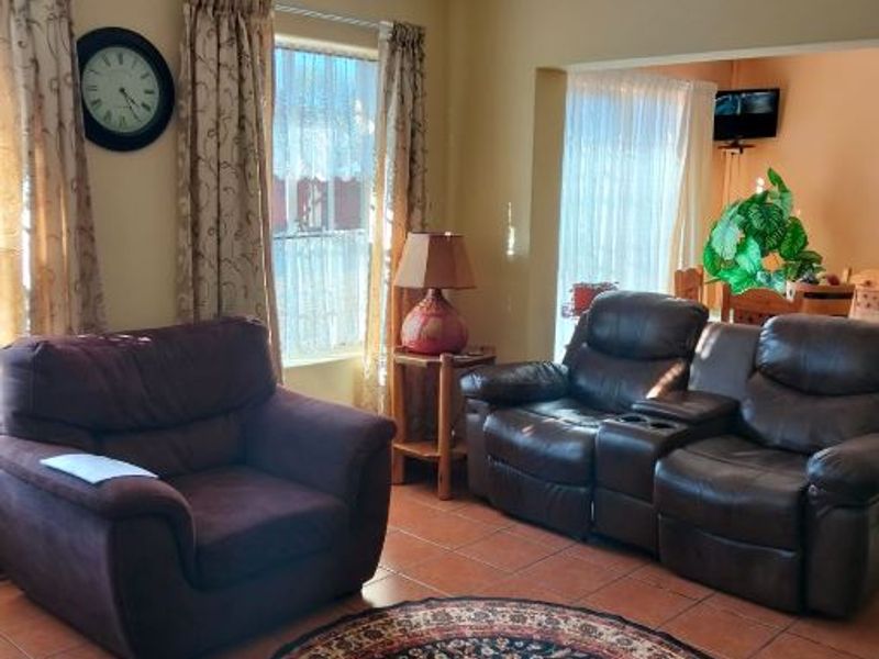 A comfortable living room featuring tiled flooring and coved ceilings, with an open-plan flow leading into an adjacent dining area.