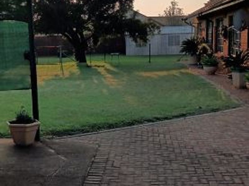 A spacious rear garden featuring a brick-paved patio area, a well-maintained lawn, and a mature tree, providing a peaceful outdoor setting.