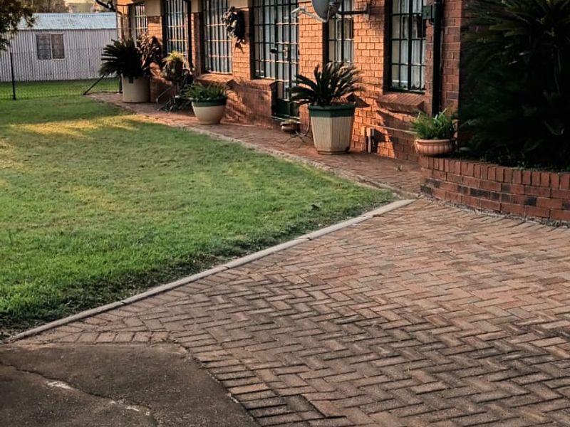 Rear view of the house featuring a brick facade, tiled roof, and a paved driveway leading to a well-maintained garden area.