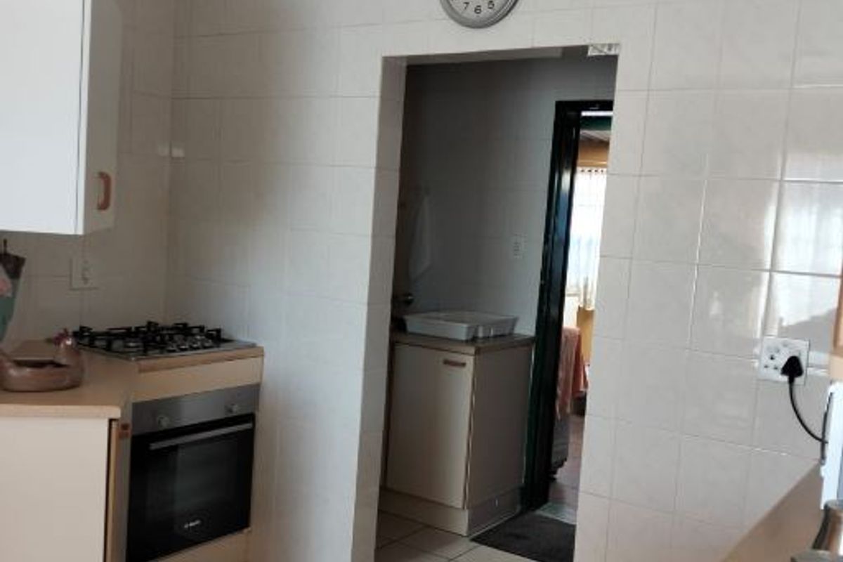 A functional kitchen featuring tiled walls, laminate countertops, and a built-in oven with gas hob, leading into a secondary utility or scullery area.