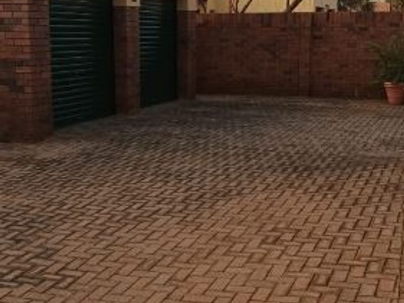 A double garage with roller shutter doors and extensive brick-paved driveway area.