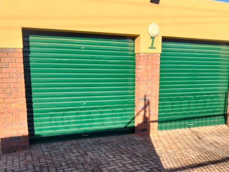 A double garage featuring green roller doors, brick masonry detailing, and a paved driveway area.
