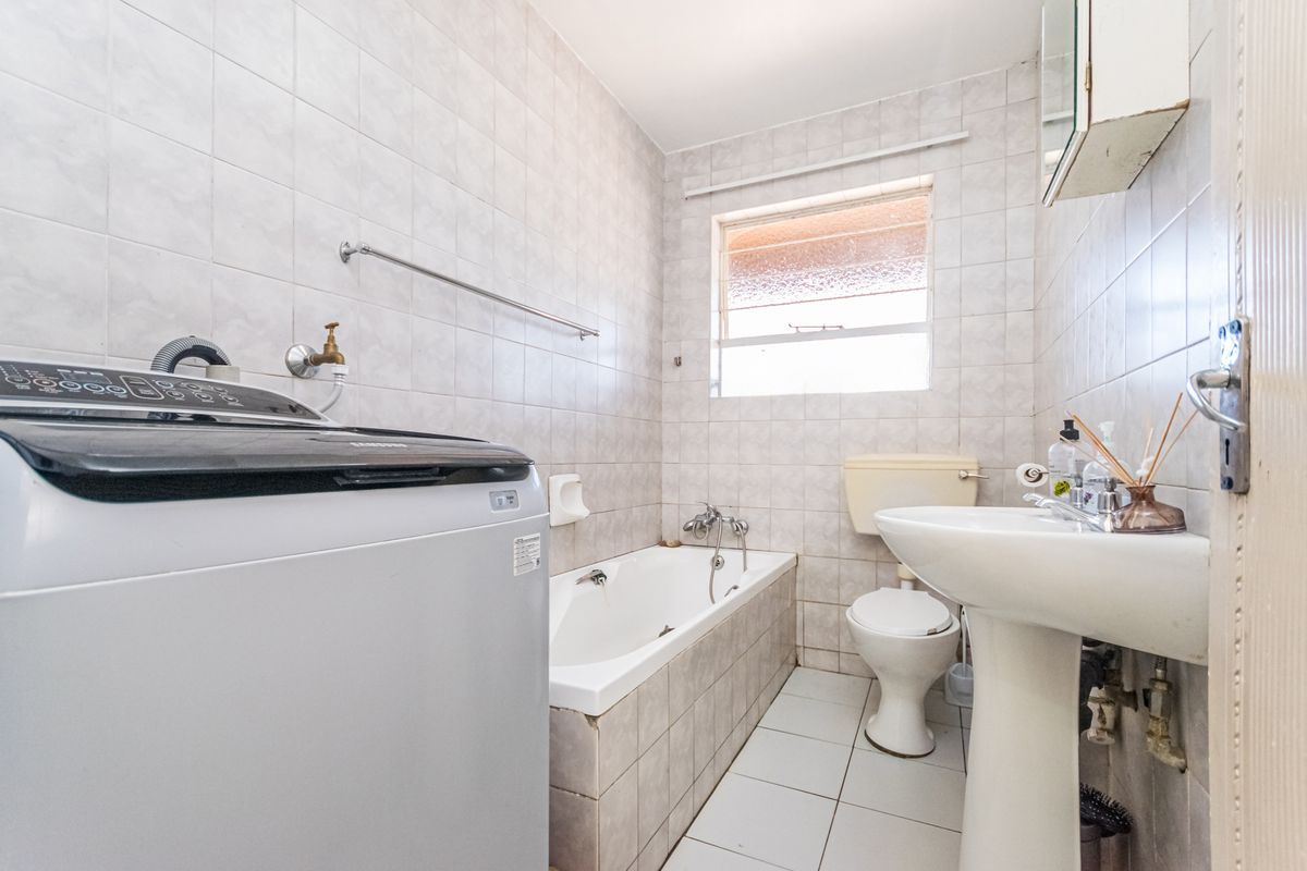 A functional bathroom featuring a bathtub, pedestal basin, and toilet with tiled finishes. The space includes plumbing connections for a washing machine.