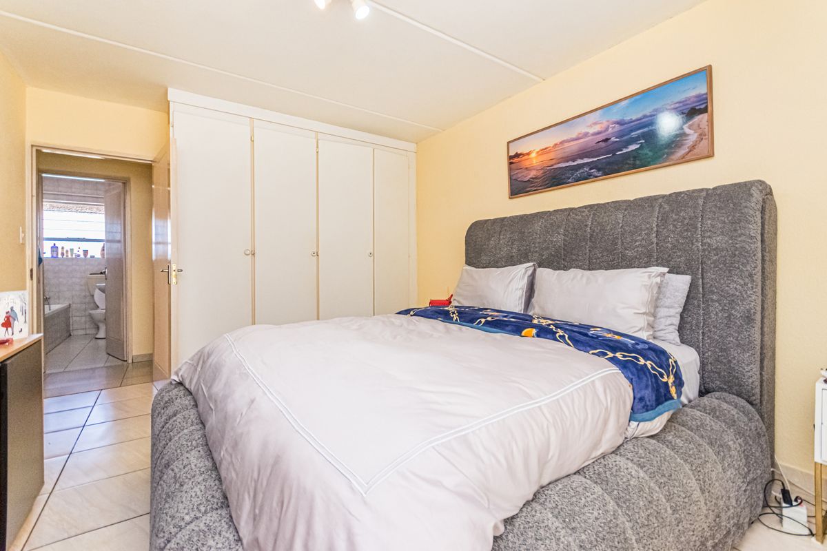 A bedroom featuring built-in cupboards and tiled flooring, with an adjoining bathroom visible through the doorway.